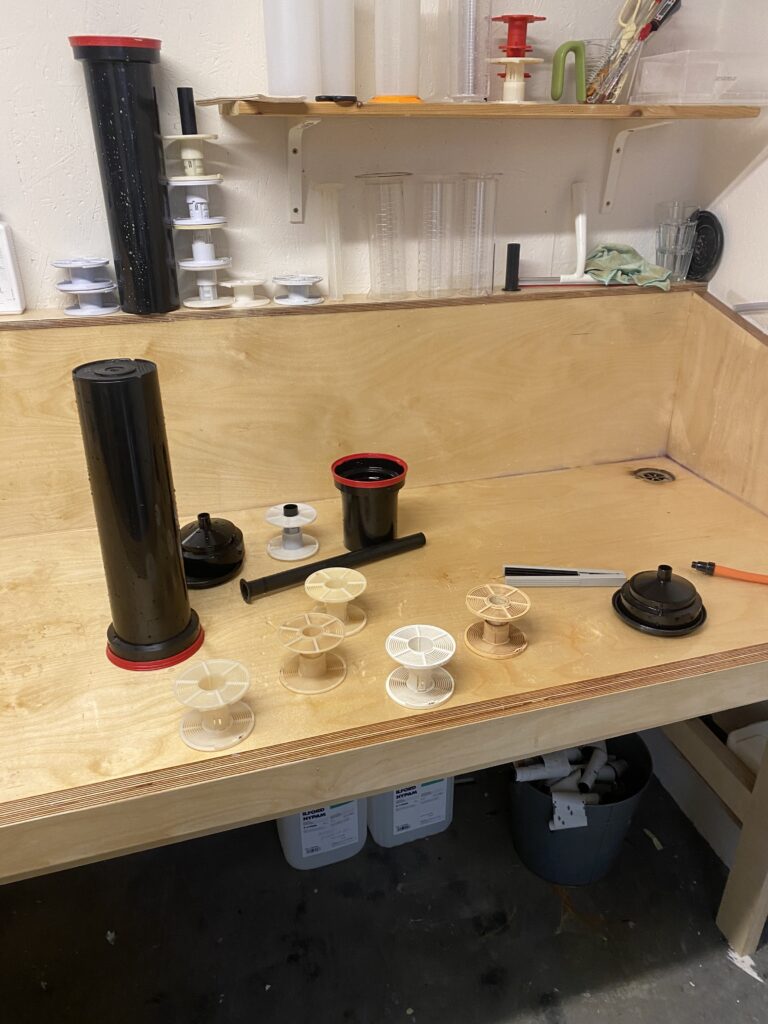 A wooden darkroom sink filled with an empty developing tanks, six reels and a squeegee