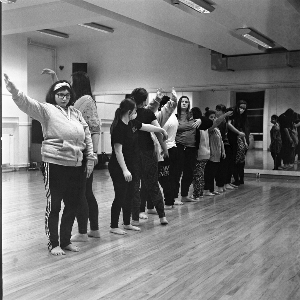 A black and white photo of a group of dancers stood in a line, several of the have their hands in the air